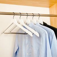 white shirts hung on a modern white wooden hangers with black chrome non slip pant bar and black chrome 360 degree hook, minimalist capsule wardrobe design with white hangers with black chrome hardware.