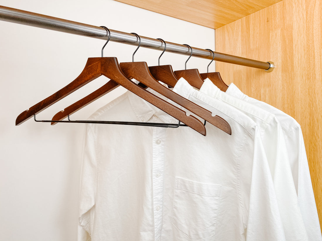 white shirts hung on a modern retro or dark brown wooden hangers with black chrome non slip pant bar and black chrome 360 degree hook, minimalist capsule wardrobe design with retro or dark brown hangers with black chrome hardware.