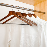 white shirts hung on a modern retro or dark brown wooden hangers with black chrome non slip pant bar and black chrome 360 degree hook, minimalist capsule wardrobe design with retro or dark brown hangers with black chrome hardware.