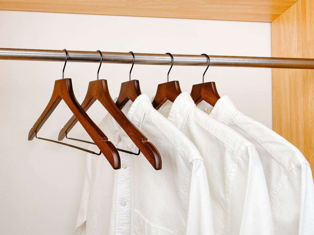 white shirts hung on a modern retro or dark brown wooden hangers with black chrome non slip pant bar and black chrome 360 degree hook, minimalist capsule wardrobe design with retro or dark brown hangers with black chrome hardware.