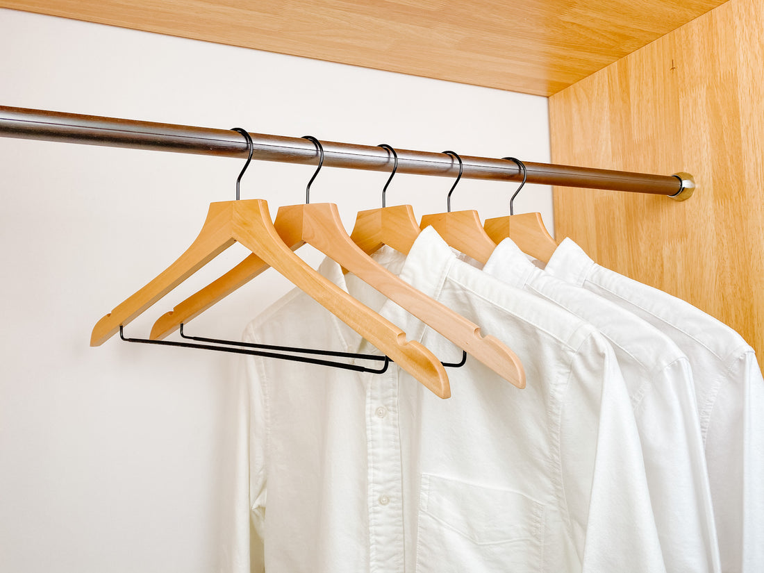 white shirts hung on a modern natural wooden hangers with black chrome non slip pant bar and black chrome 360 degree hook, minimalist capsule wardrobe design with natural hangers with black chrome hardware.