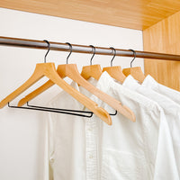 white shirts hung on a modern natural wooden hangers with black chrome non slip pant bar and black chrome 360 degree hook, minimalist capsule wardrobe design with natural hangers with black chrome hardware.