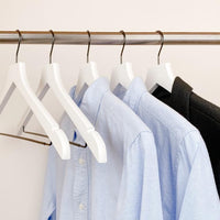 white shirts hung on a modern white wooden hangers with black chrome non slip pant bar and black chrome 360 degree hook, minimalist capsule wardrobe design with white hangers with black chrome hardware.