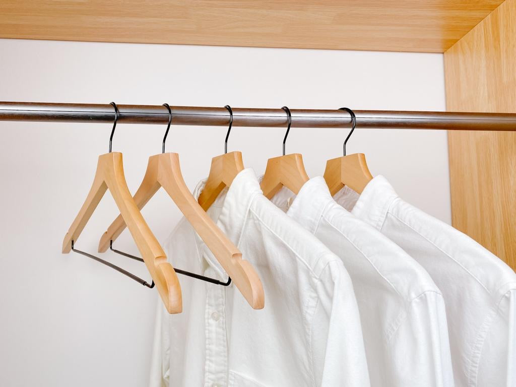 white shirts hung on a modern natural wooden hangers with black chrome non slip pant bar and black chrome 360 degree hook, minimalist capsule wardrobe design with natural hangers with black chrome hardware.