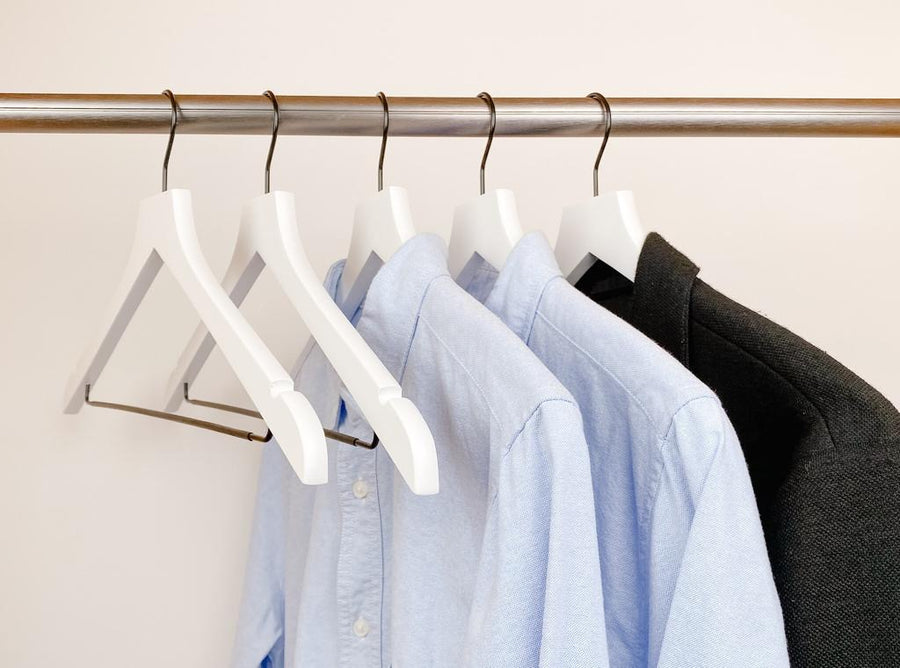 white shirts hung on a modern white wooden hangers with black chrome non slip pant bar and black chrome 360 degree hook, minimalist capsule wardrobe design with white hangers with black chrome hardware.